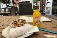 a burrito sitting on top of a white plate next to a bottle of orange juice