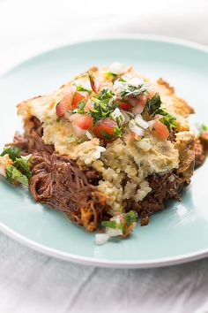 a blue plate topped with meat and veggies on top of mashed potatoes