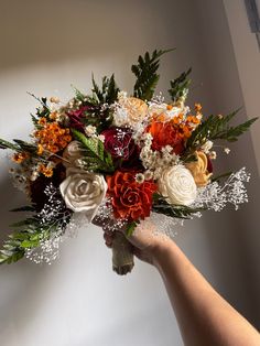 a bouquet of flowers is being held up by someone's hand in front of a white wall