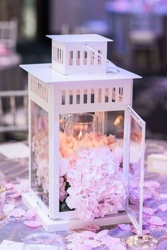 a small white lantern with flowers inside it on a table covered in pink and white confetti