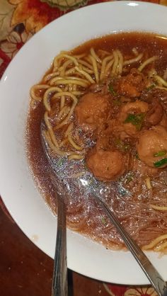 a white plate topped with pasta and meat covered in gravy on top of a wooden table