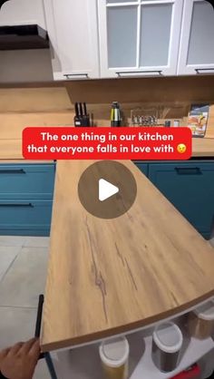 a person is writing on a wooden counter top in a kitchen with blue cabinets and white cupboards