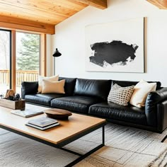 a living room with black leather couches and white walls, wood ceilinging and large windows