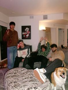 a group of young men sitting on top of a bed next to a brown and white dog