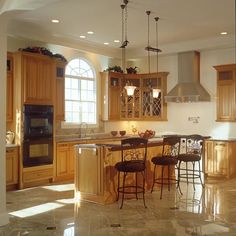 a large kitchen with wooden cabinets and an island in the middle is lit by two pendant lights