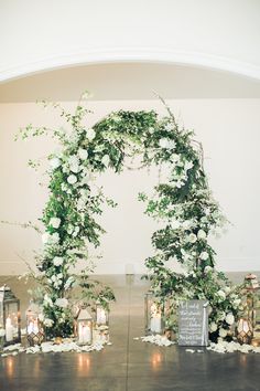 a table topped with lots of candles and flowers next to an arch covered in greenery