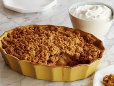 a pie sitting on top of a table next to a bowl of whipped cream and a cup