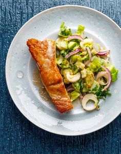 a white plate topped with fish and salad on top of a blue table cloth next to a fork