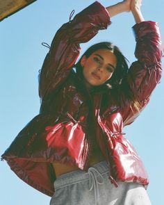 a woman wearing a red jacket and grey sweatpants is posing for the camera with her hands on her head