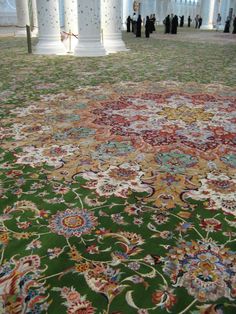 a large rug in the middle of a room with columns and people standing around it