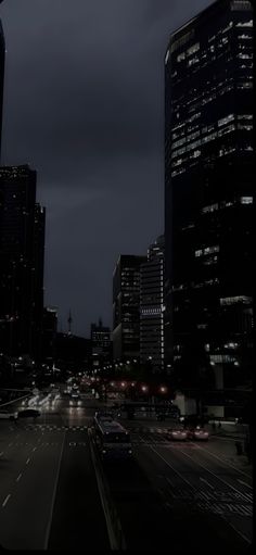 a city street at night with cars driving on the road and tall buildings in the background