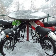 three motorbikes are parked in the snow near a table with two bikes on it