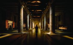 a person standing in an empty room with columns and paintings on the walls at night