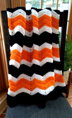 an orange and black crocheted blanket sitting on top of a chair next to a window