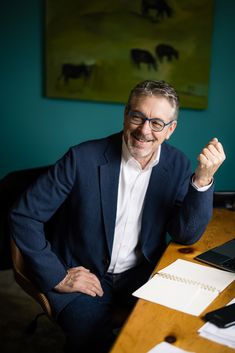 a man sitting at a desk with his hand up in the air and smiling for the camera