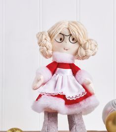 a doll with glasses and a red dress is sitting on a table next to ornaments