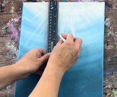 a person is drawing on a piece of blue paper with a white pencil and ruler