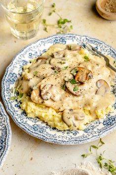 a blue and white plate topped with mashed potatoes covered in mushroom gravy