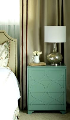 a bedroom with a green dresser next to a white bed and a lamp on top of it