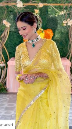 a woman in a yellow sari is looking down at her cell phone and smiling