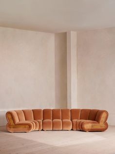 a large brown couch sitting on top of a floor next to a white wall in an empty room