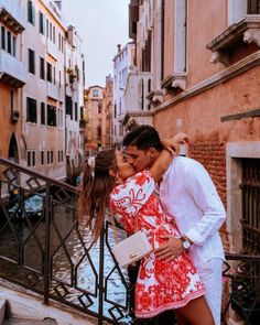 a man and woman kissing in front of some buildings on the water's edge