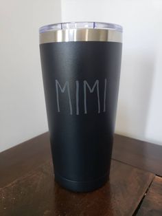 a black and silver tumbler with the word mimi written on it sitting on a wooden table