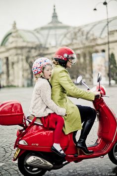 two people riding on the back of a red scooter