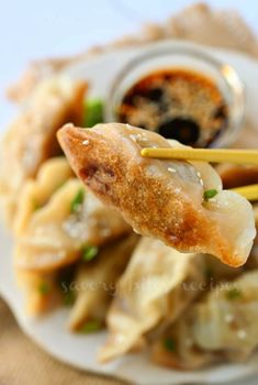 a white plate topped with dumplings covered in sauce and chopsticks on top of it