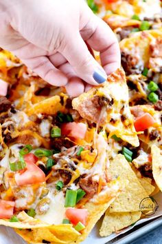 someone is dipping some tortilla sauce on top of the nachos with cheese and other toppings