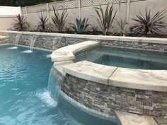 an outdoor swimming pool surrounded by stone walls and water features with plants in the background