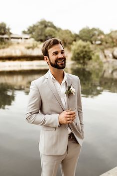 a man in a suit standing next to the water with his hand on his hip