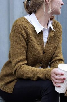 a woman sitting on the ground holding a coffee cup and wearing a brown cardigan