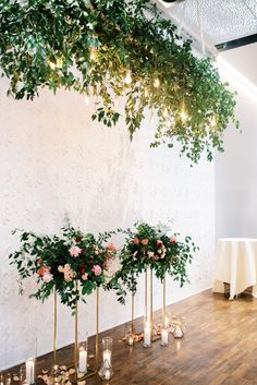 an arrangement of greenery and candles are arranged on the floor in front of a white wall