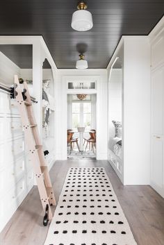 a white hallway with black and white rugs on the floor next to a ladder