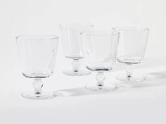 four clear glasses are lined up on a white surface