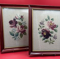 two framed cross - stitch pictures with flowers on them are sitting next to each other