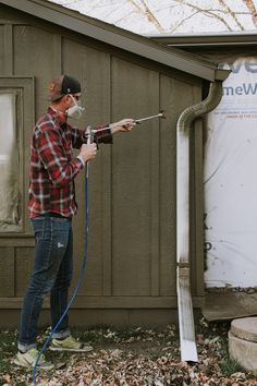 a man in plaid shirt spraying water from a hose on the side of a house