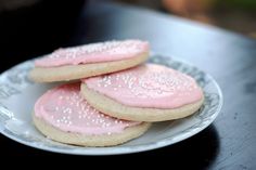 three cookies with pink frosting on a white and gray plate sitting on a black table