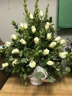 a vase filled with white roses on top of a wooden table next to a green plant