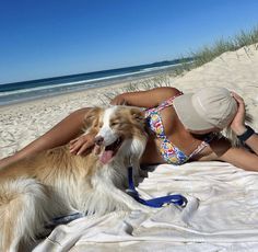 a woman laying on top of a sandy beach next to a brown and white dog