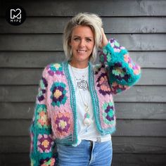 a woman wearing a colorful crocheted cardigan and smiling at the camera with her hand on her head