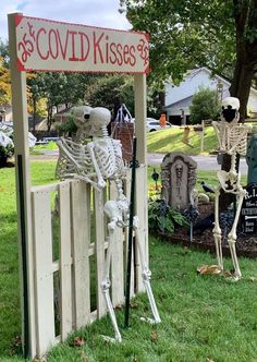 two skeleton statues sitting in front of a sign that says good kiss's on it