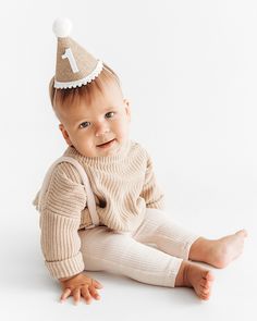 a baby wearing a birthday hat sitting on the floor