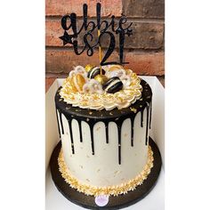 a white and black cake with gold sprinkles is on a table next to a brick wall