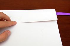 a hand is holding a piece of white paper with a purple ribbon on the edge