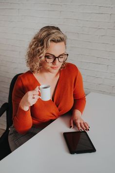 a woman sitting at a table holding a cup and tablet