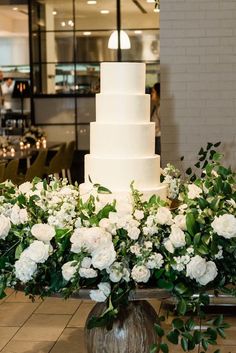 a large white cake sitting on top of a table next to flowers and greenery