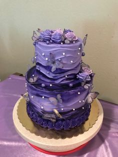 a three tiered cake with purple frosting and butterflies on top is sitting on a table