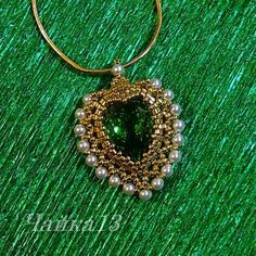 a necklace with pearls and a green beaded pendant on a green surface, close up